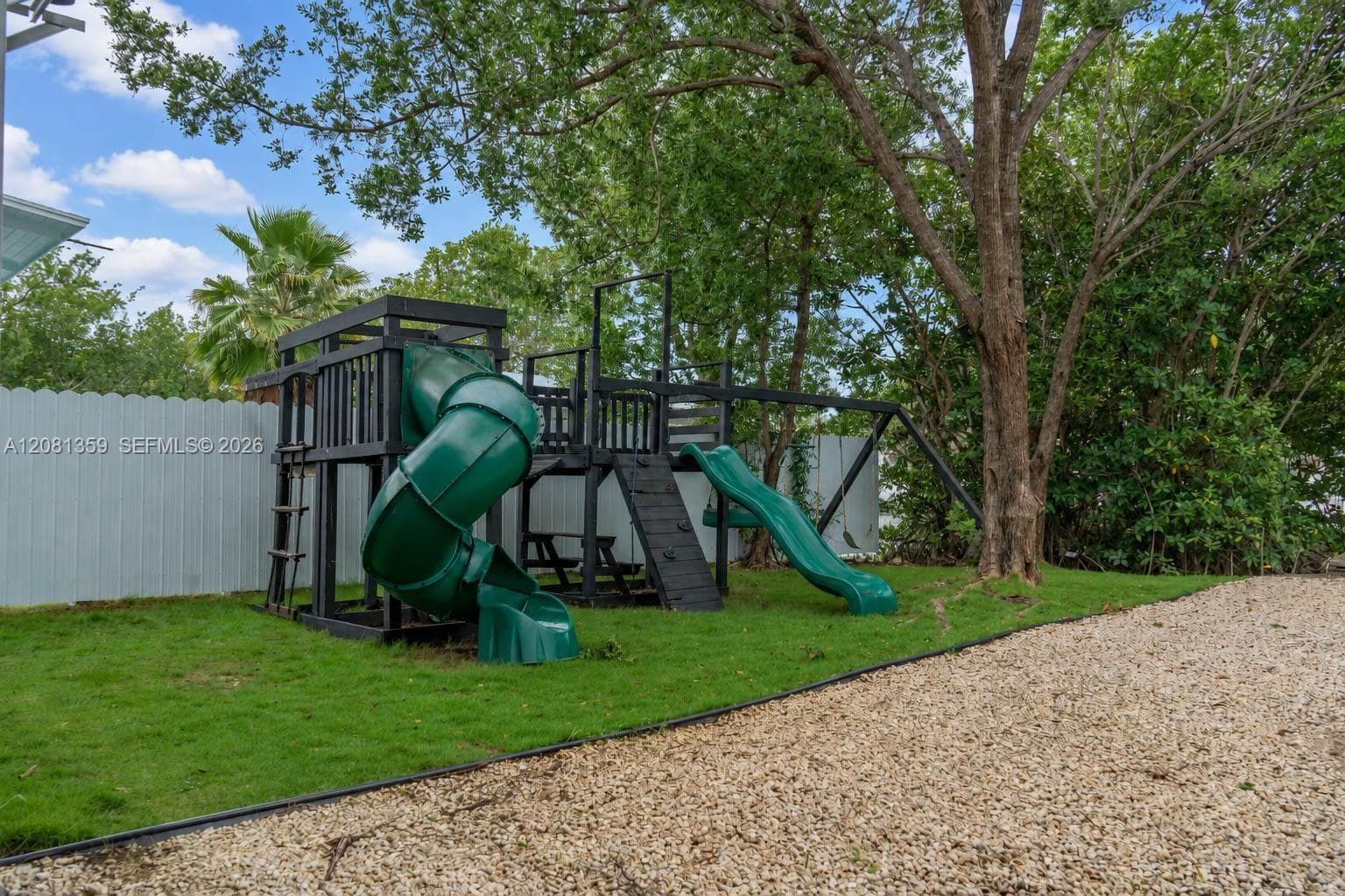 Backyard featuring a manicured lawn, stone ground cover, perimeter fencing, and mature trees