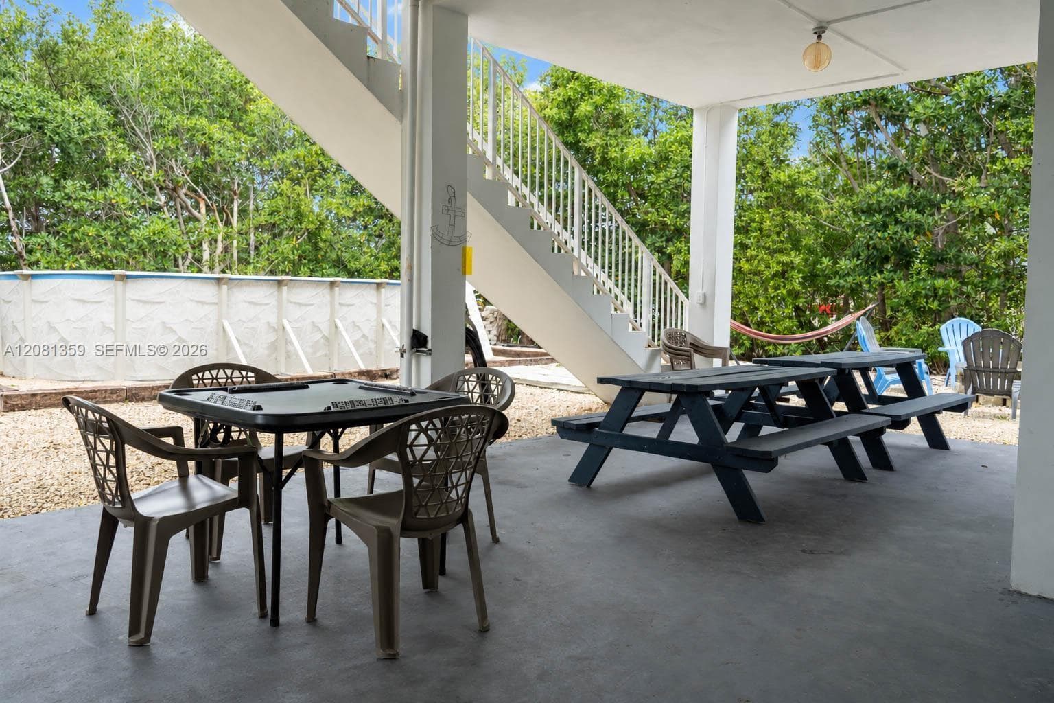 Covered ground-level patio with painted concrete flooring, exterior staircase, and exposed structural columns