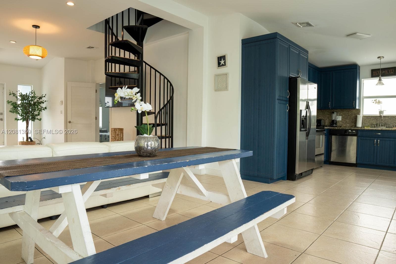 Black metal spiral staircase, blue custom cabinetry, stainless steel appliances, and ceramic tile flooring