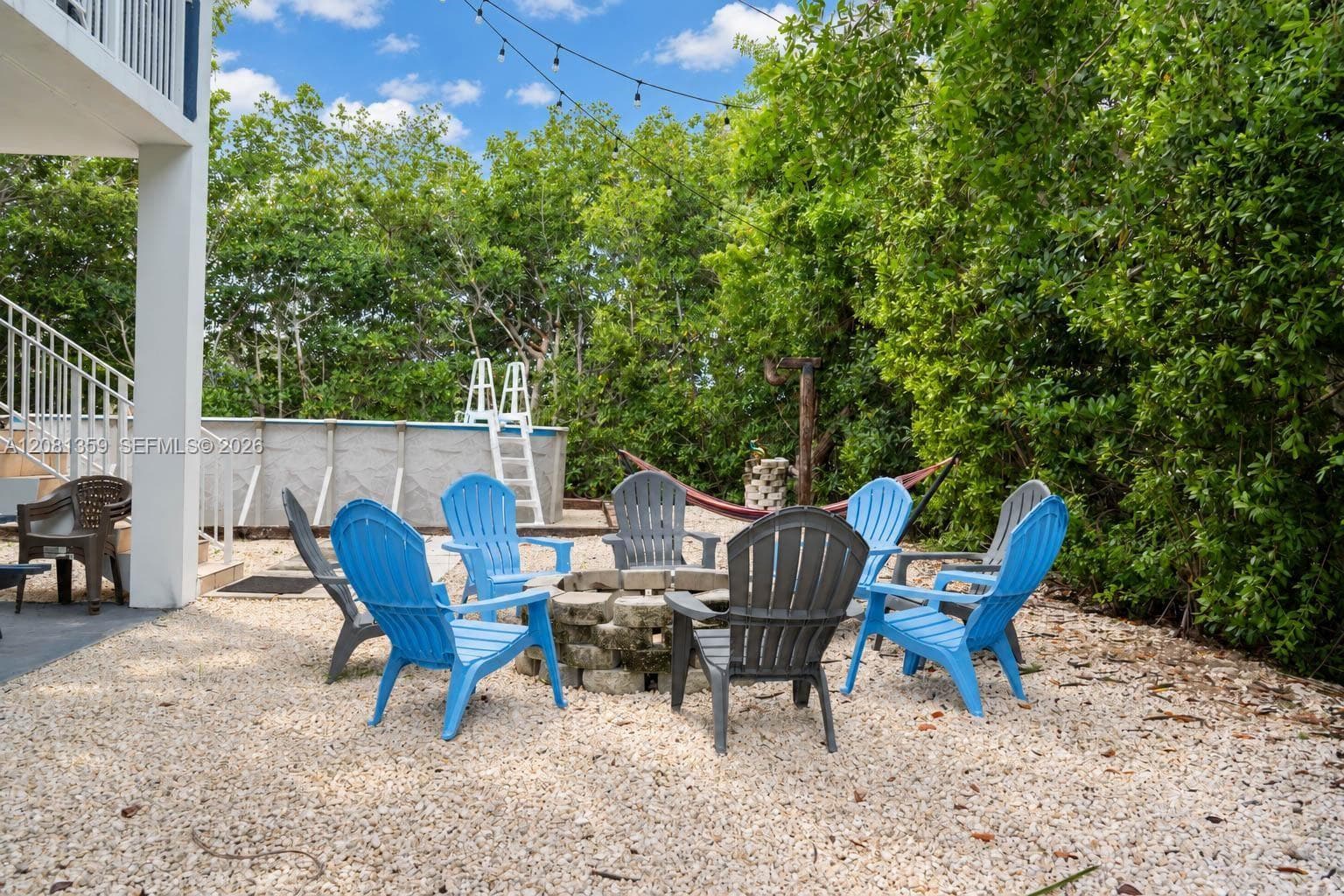 Outdoor area featuring a stone fire pit, gravel ground cover, overhead string lighting, and an above-ground pool