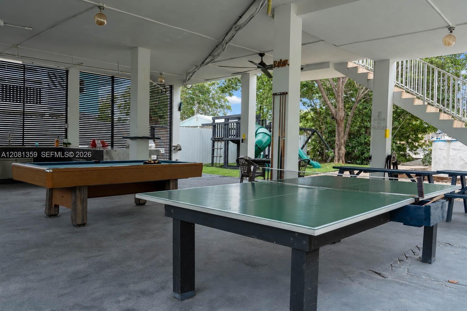 Covered outdoor patio featuring concrete flooring, built-in outdoor kitchen, recessed ceiling lighting, and staircase