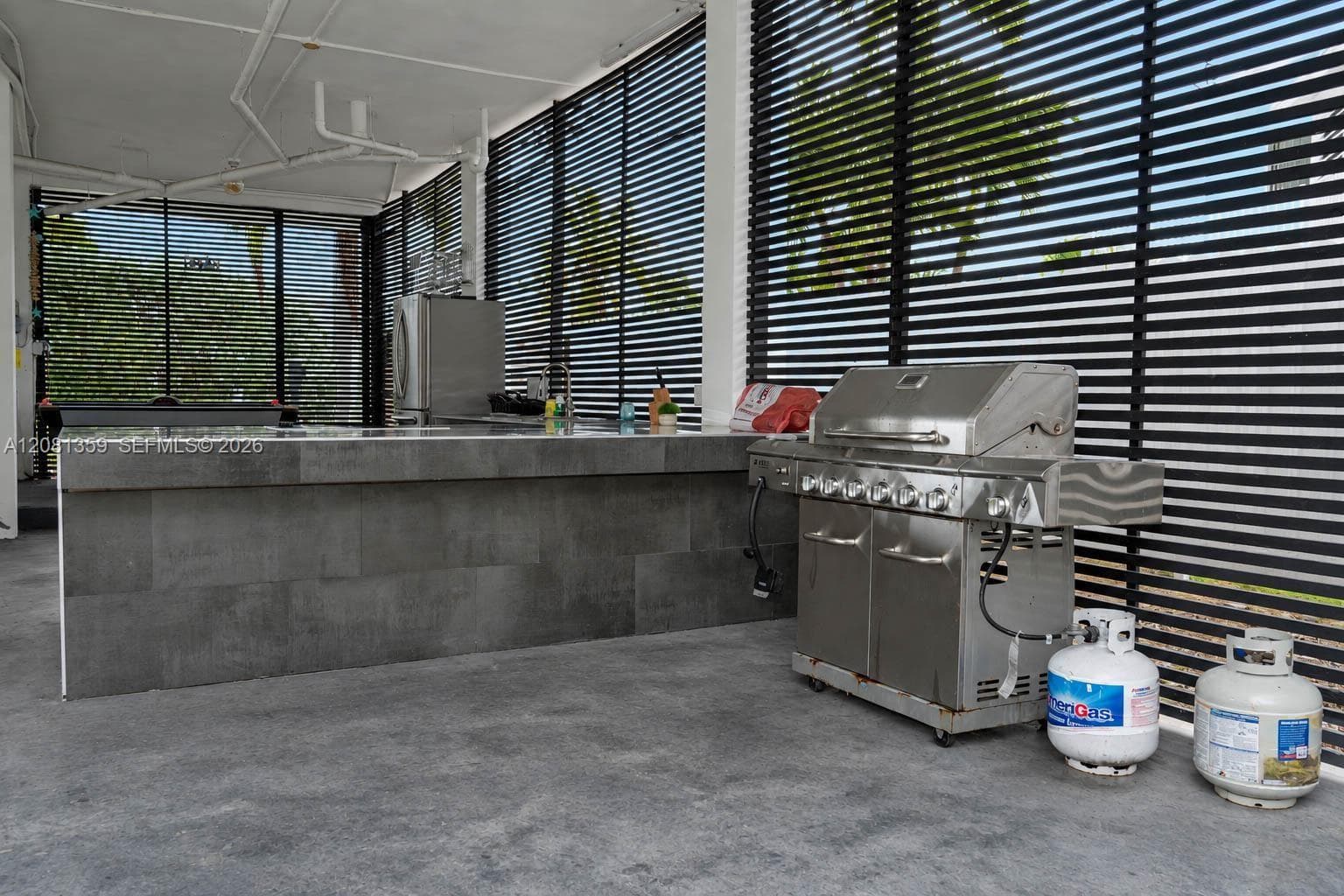 Outdoor kitchen featuring a stone-faced island, stainless steel grill, and horizontal slat privacy screening