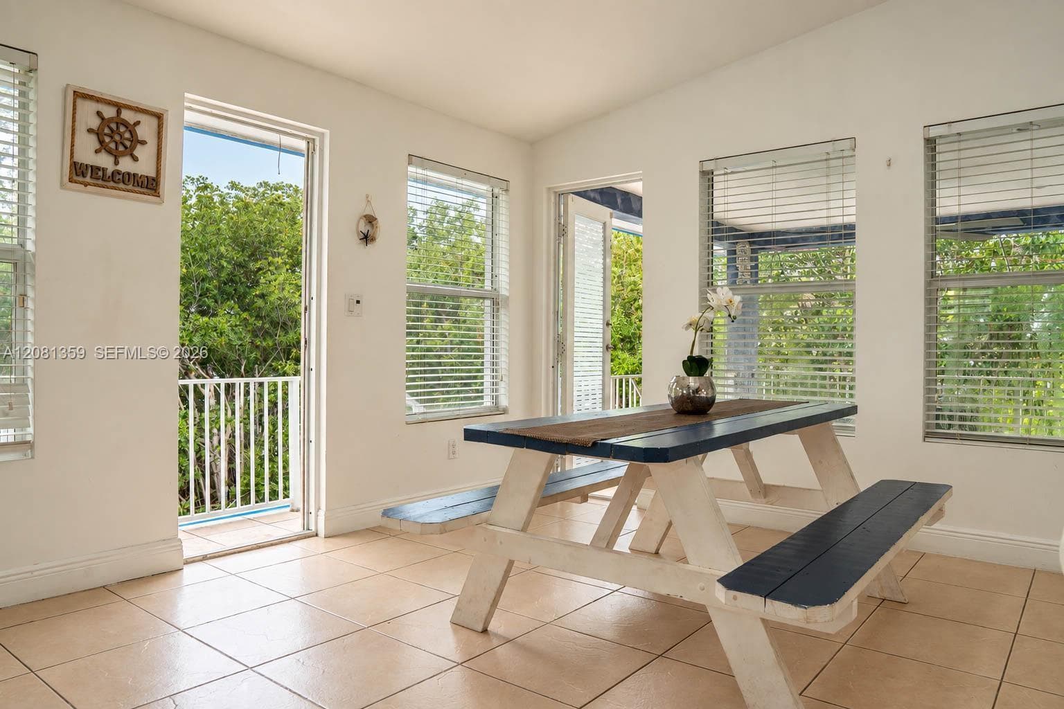 Light-filled room featuring neutral ceramic tile flooring, multiple windows with horizontal blinds, and dual access points to exterior balconies