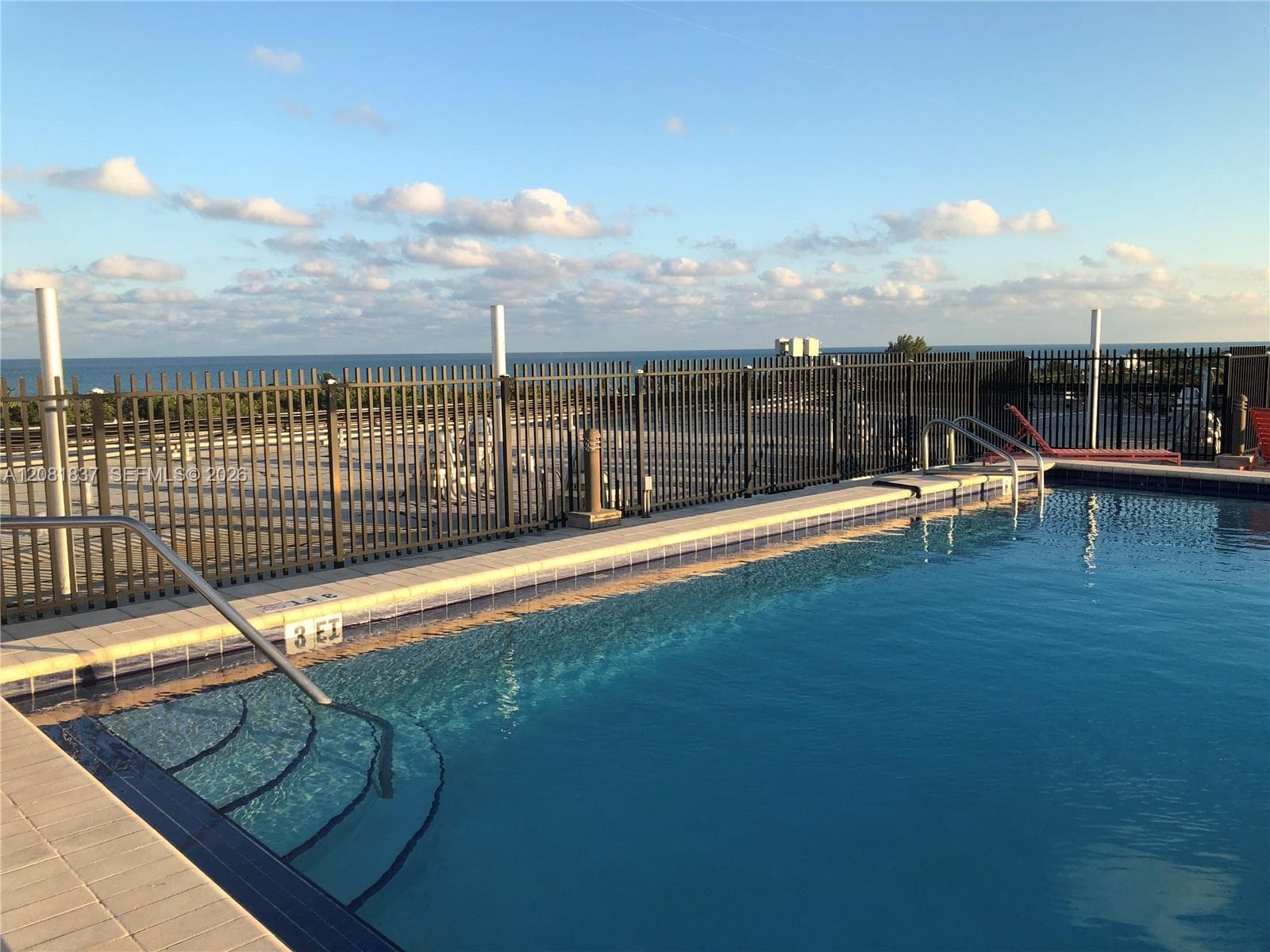 In-ground swimming pool featuring a tiled waterline, metal safety fencing, integrated entry steps, and stainless steel handrails