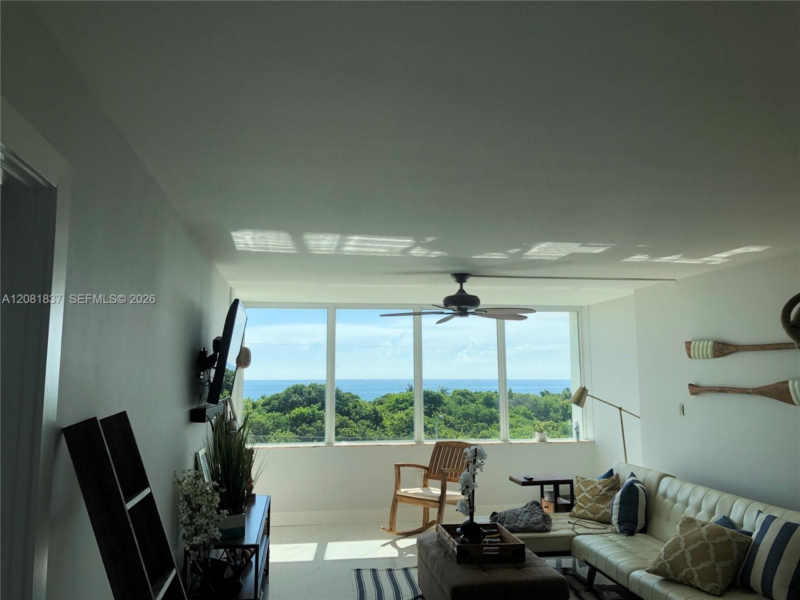 Floor-to-ceiling windows featuring ocean and treeline scenery, accompanied by an attached ceiling fan