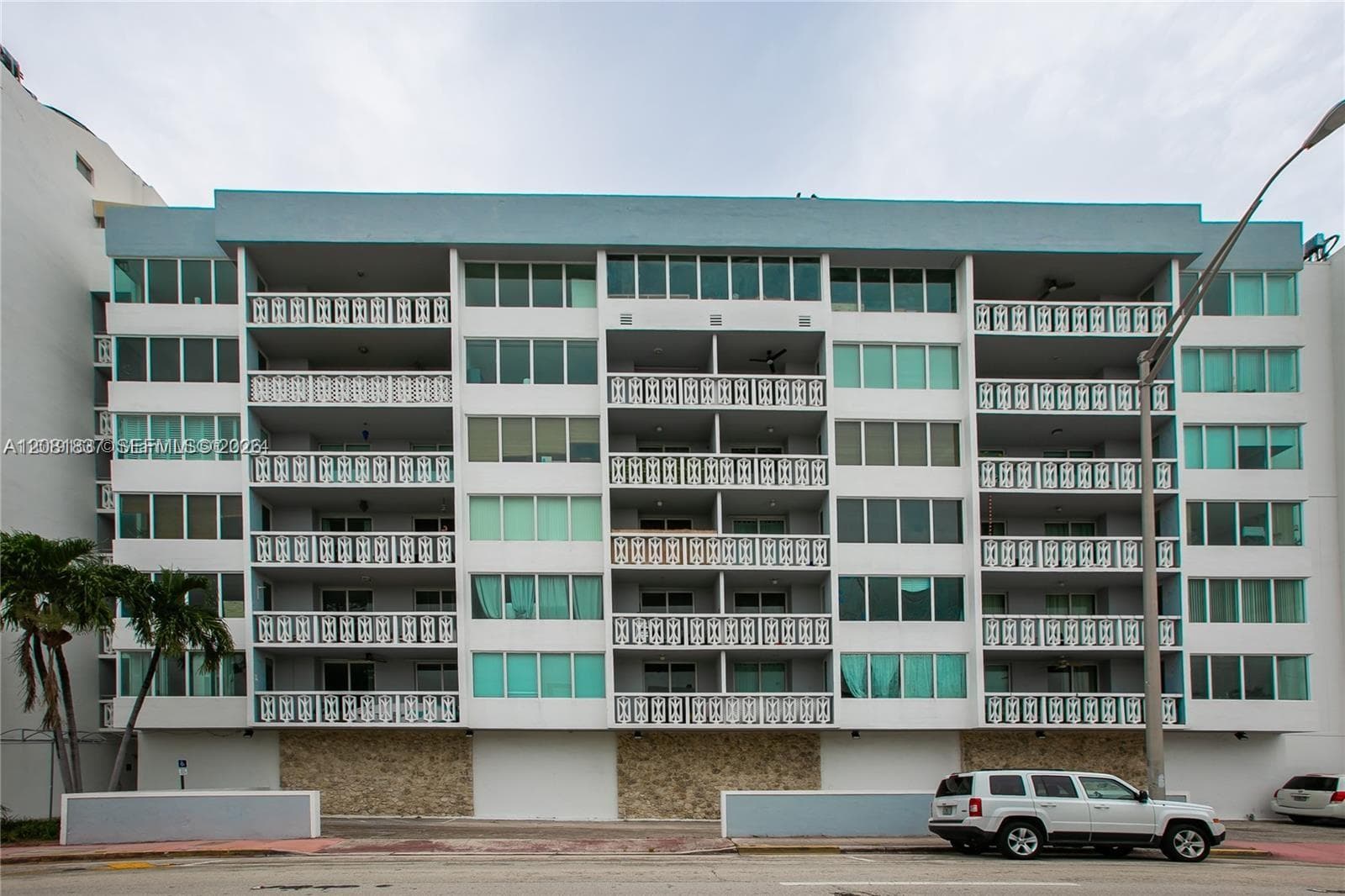 Multi-story residential building exterior featuring a stone-clad ground level, repetitive rhythmic balconies with patterned railings, and floor-to-ceiling glass fenestration