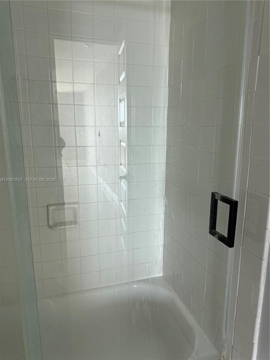 Shower enclosure featuring floor-to-ceiling white square tile, a built-in recessed soap niche, a frameless glass door, and a matte black square handle