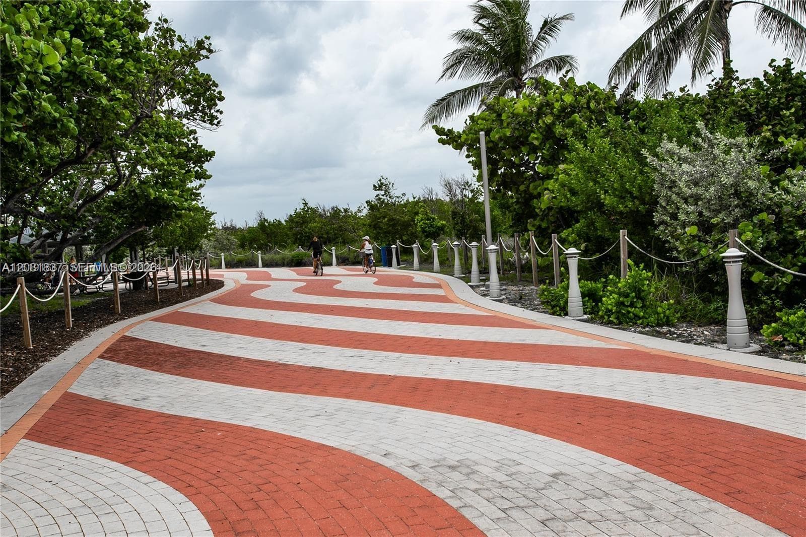Winding paved walkway featuring a decorative two-tone brick pattern, bordered by integrated bollard lighting, rope-style railings, and native tropical landscaping