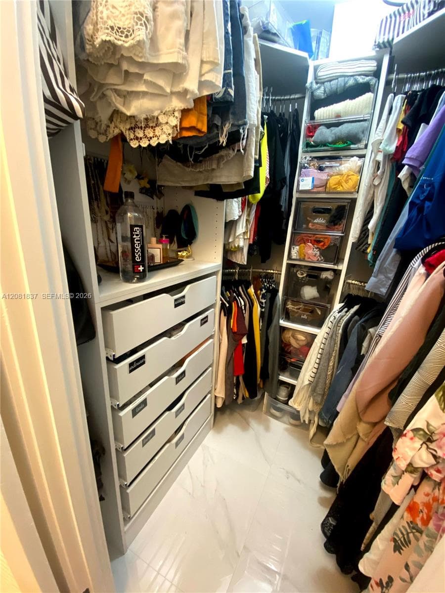 Walk-in closet featuring white built-in cabinetry, custom drawer stack, integrated shelving, and stone-finish flooring