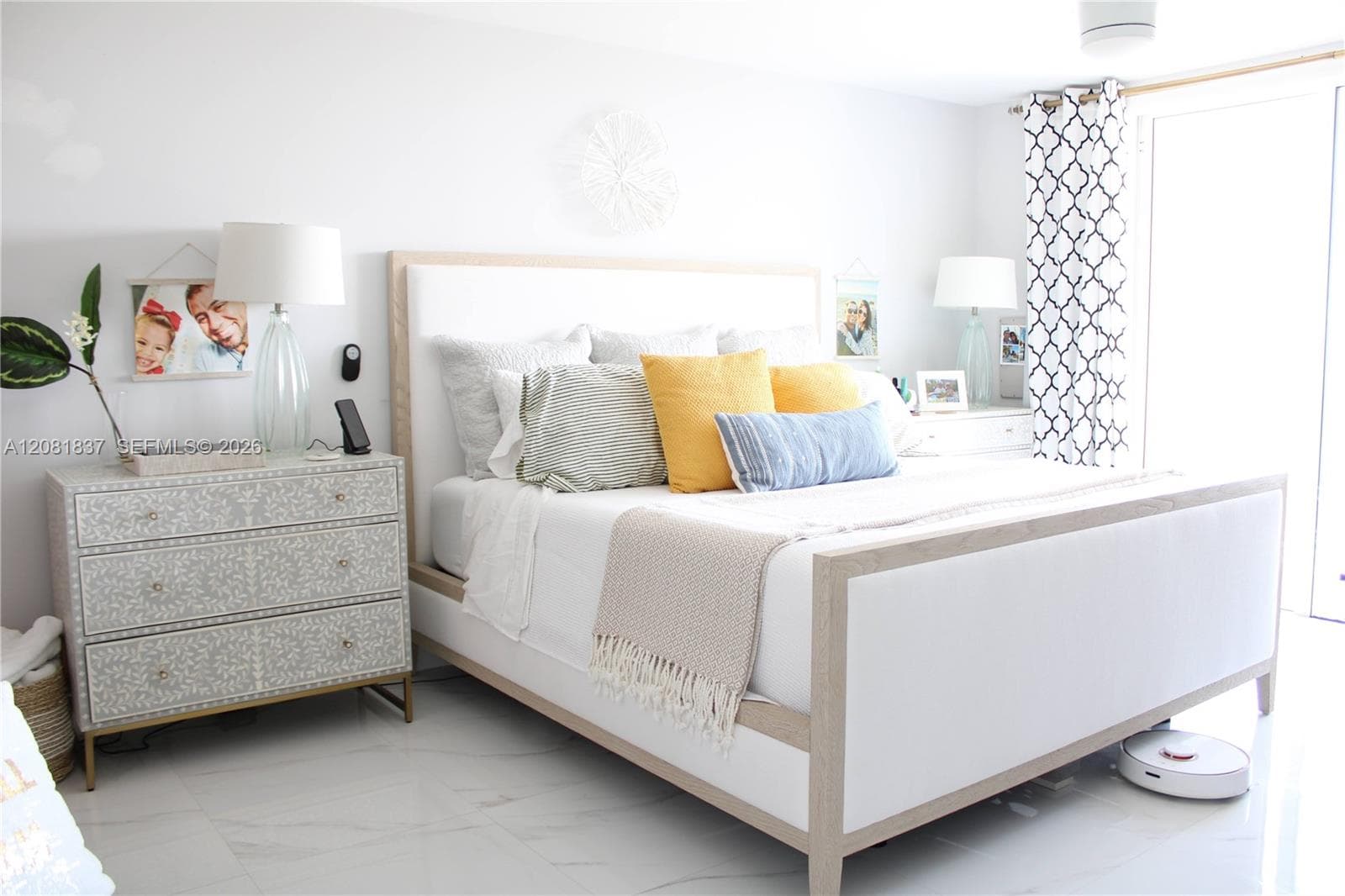 Light-filled bedroom featuring large-format polished tile flooring and a sliding glass door with patterned drapery