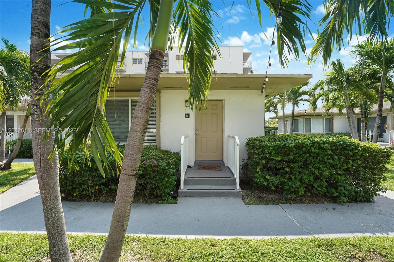 Exterior façade featuring light-colored stucco siding, a flat roofline, concrete entry steps with white metal handrails, and mature palm trees