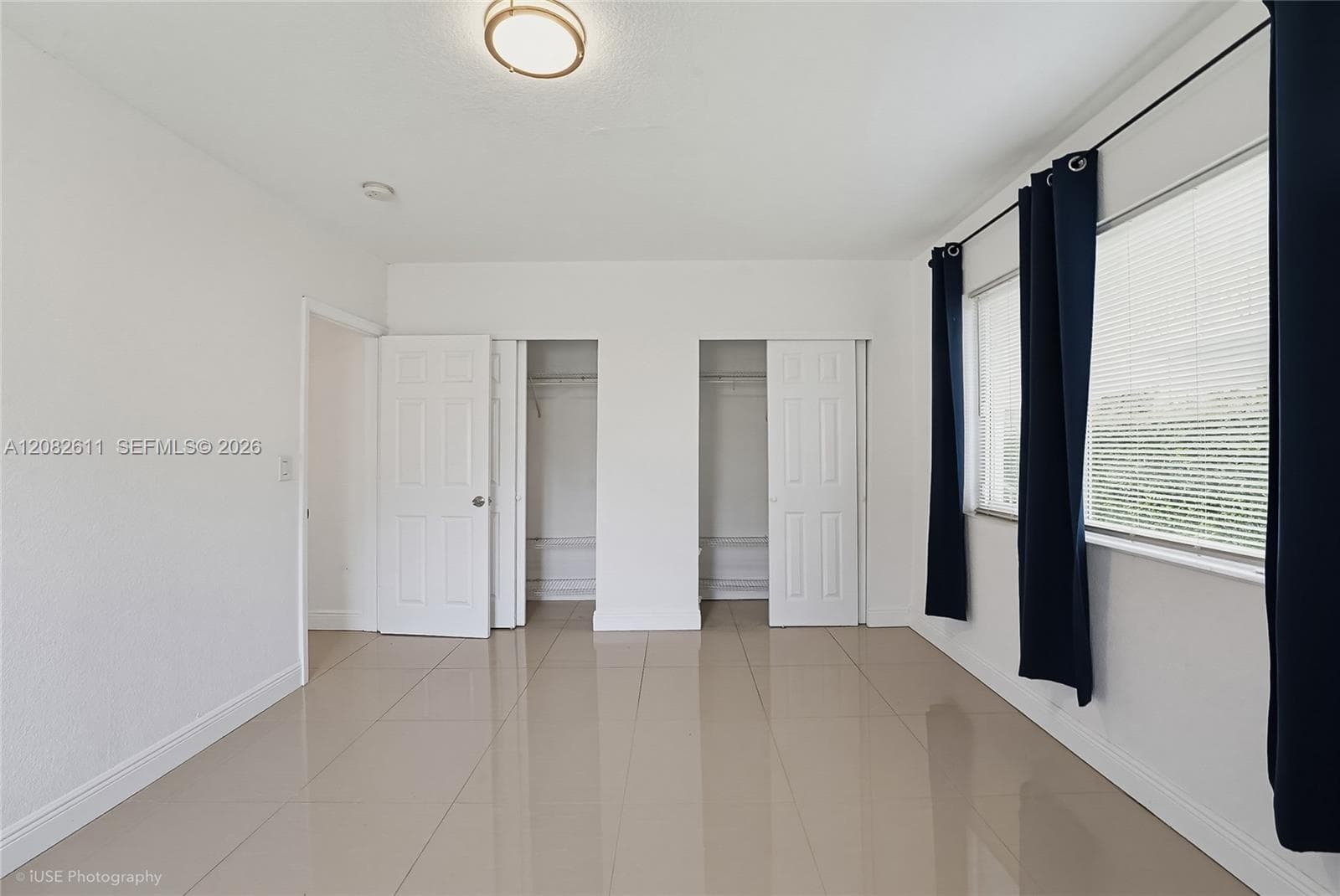 Room featuring large-format tile flooring, dual closets with swinging doors, multi-pane windows, and a flush-mount ceiling light fixture