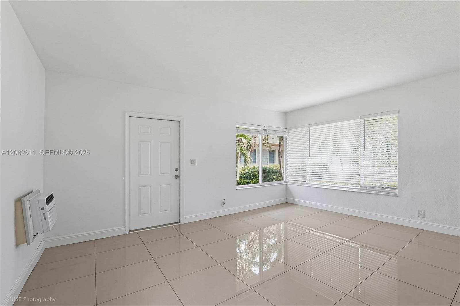 Neutral interior featuring polished large-format tile flooring, a six-panel entry door, and expansive windows fitted with horizontal blinds