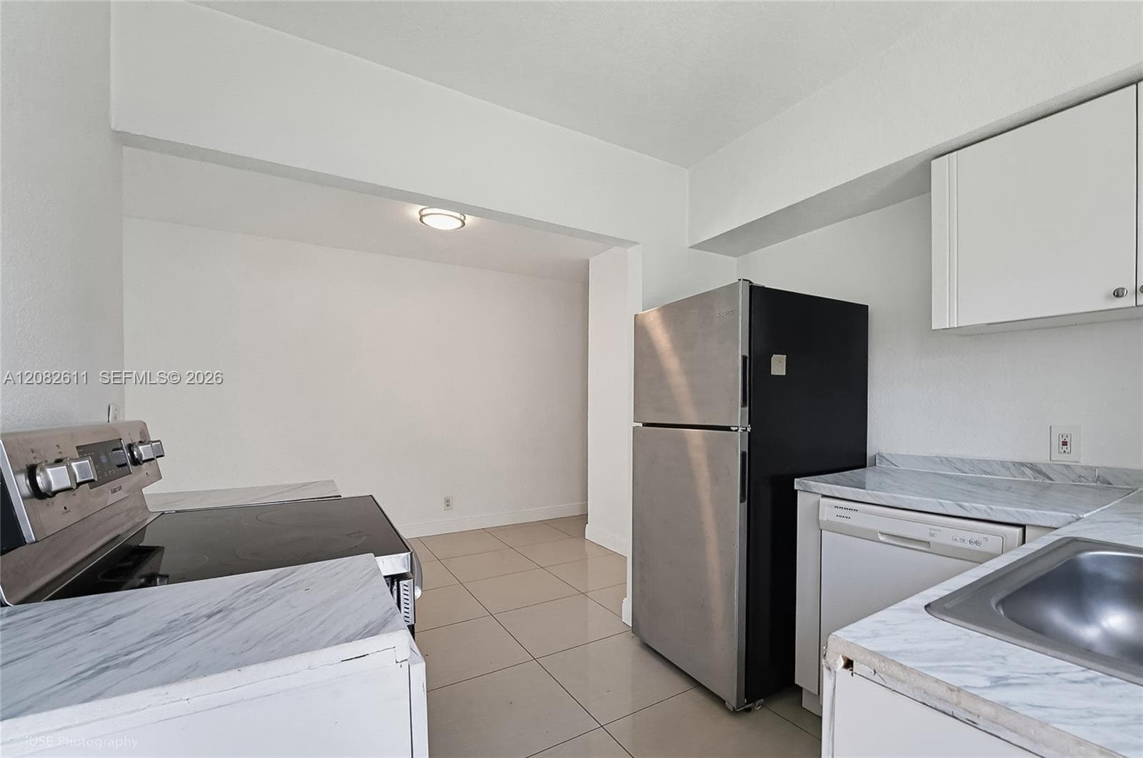 Kitchen featuring white cabinetry, stone-patterned laminate countertops, large-format tile flooring, and stainless steel refrigerator