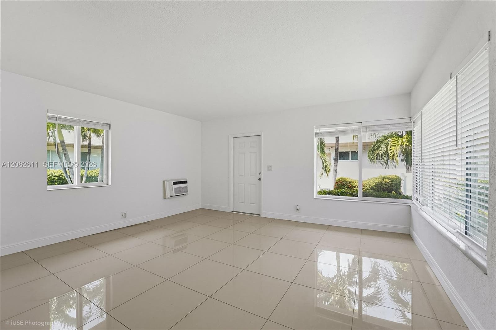 Polished tile flooring, neutral wall finishes, multiple windows, built-in wall air conditioning unit, and white paneled entry door