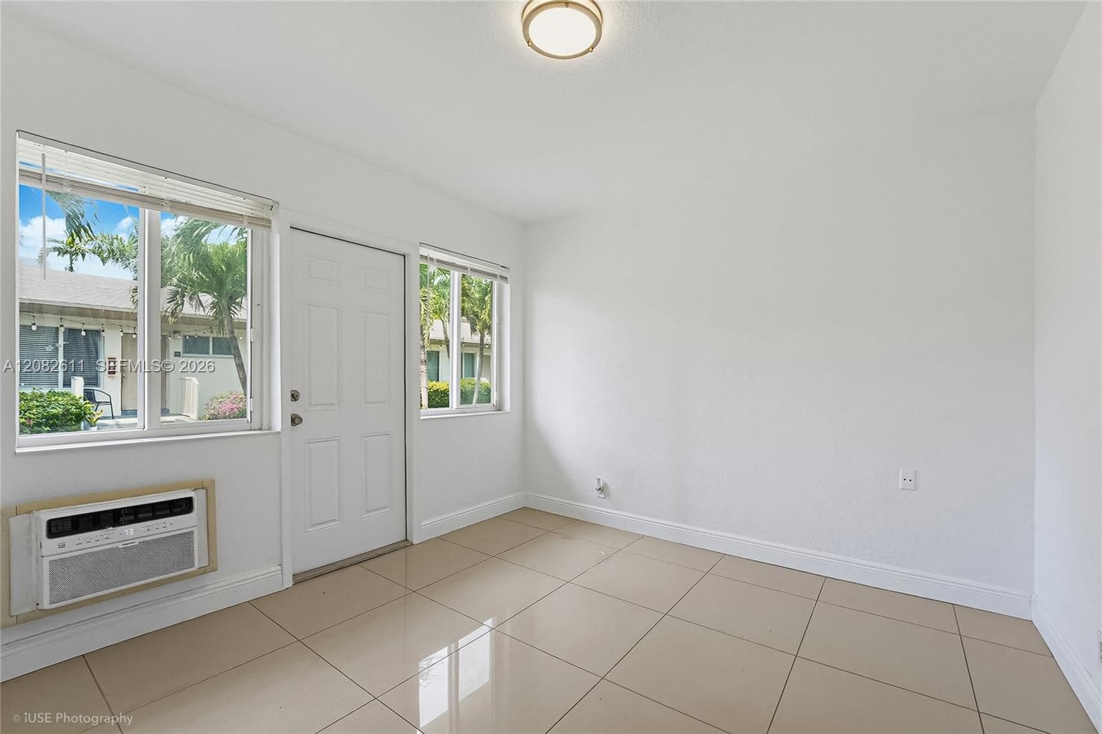 Neutral-toned ceramic tile flooring, two double-hung windows, solid-panel entry door, and wall-mounted air conditioning unit
