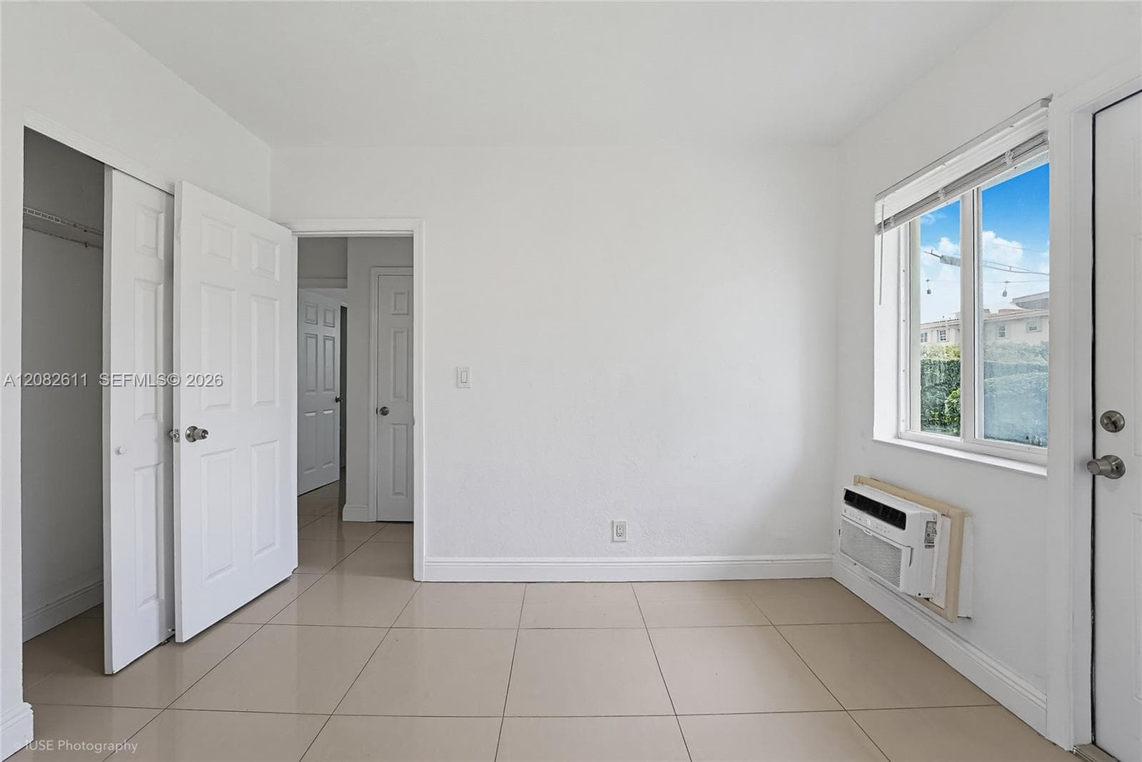 Interior room featuring large-format tile flooring, dual-panel interior doors, a reach-in closet, and a wall-mounted climate control unit