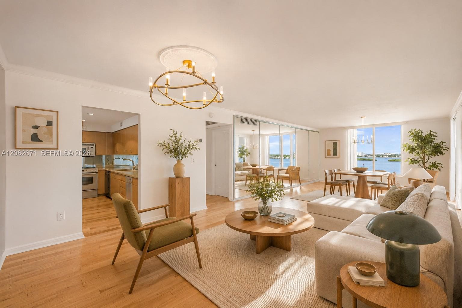 Open living and dining area, digitally staged, framed by water views and a designer chandelier.