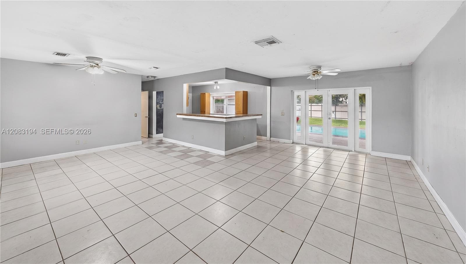Open interior featuring large-format ceramic floor tile, a built-in breakfast bar, dual ceiling fans, and glass panel doors leading to the exterior