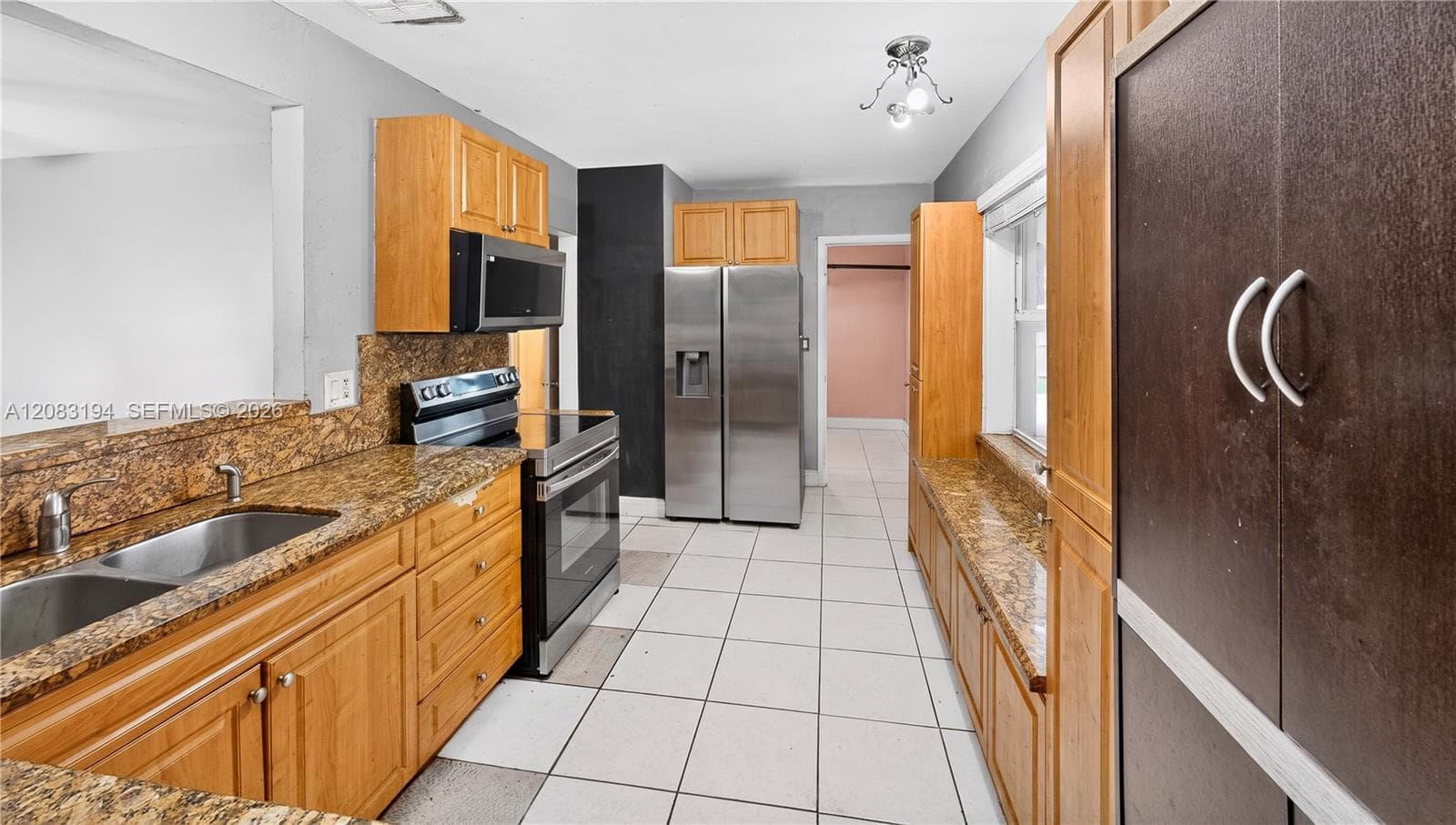 Kitchen featuring wood cabinetry, stone-finish countertops, stainless steel appliances, and ceramic tile flooring