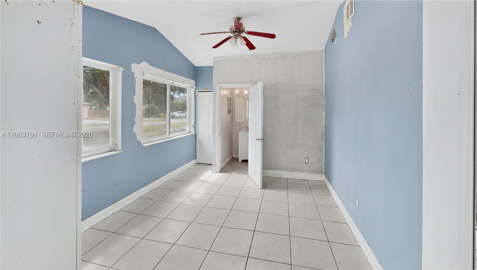 Room featuring ceramic tile flooring, vaulted ceiling with a mounted light-integrated ceiling fan, and large windows with decorative trim