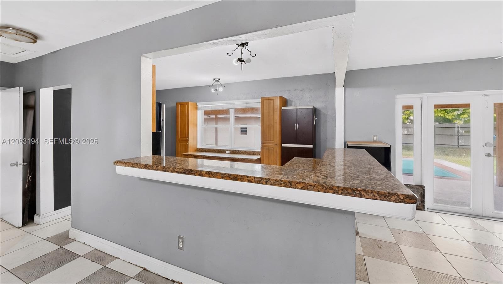 Kitchen pass-through featuring an expansive stone-surface breakfast bar, wood cabinetry, large-format tile flooring, and double glass-paned doors