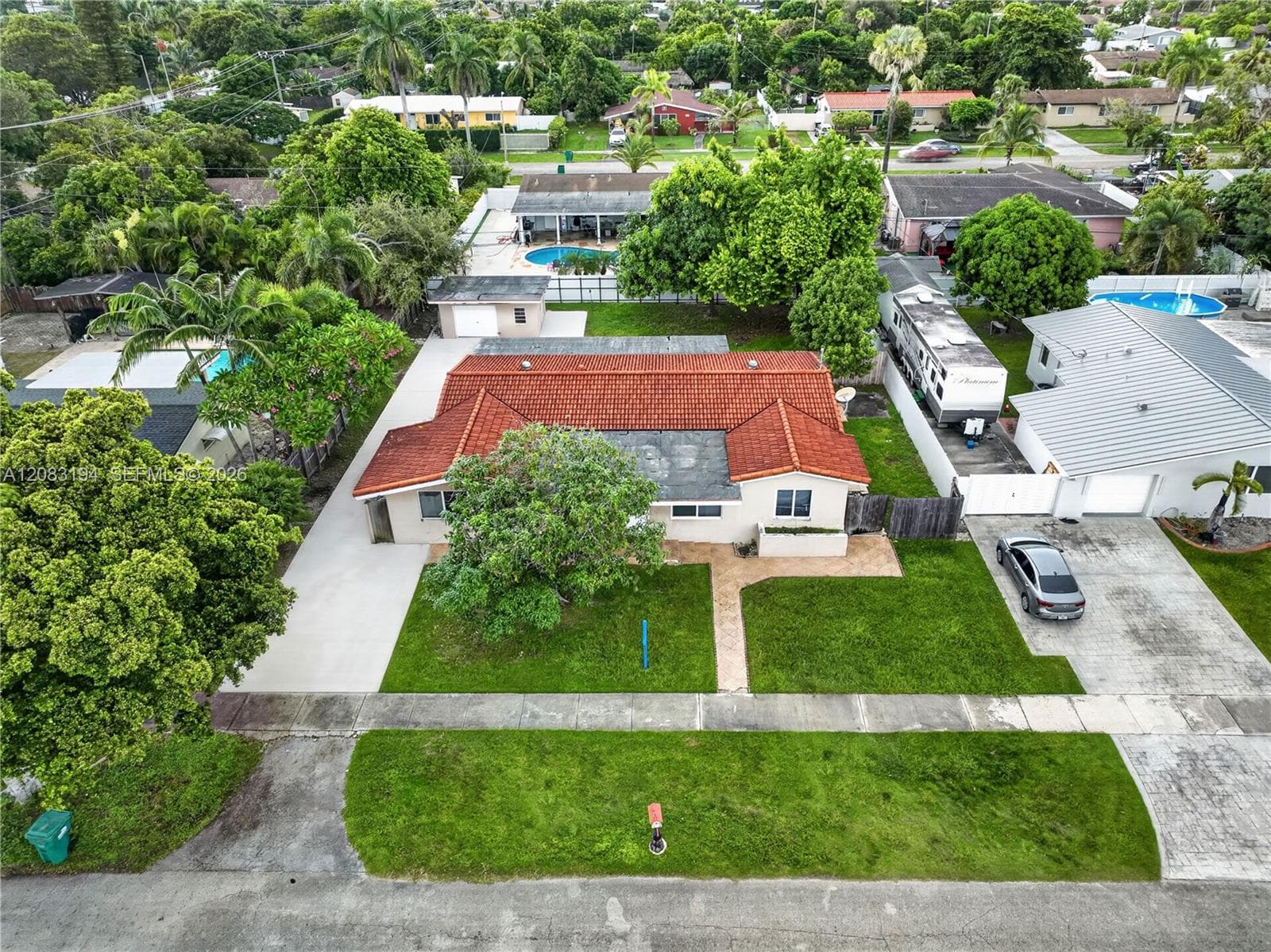 Single-story residence featuring a tile roof, concrete driveway, stone-paved walkway, and mature landscaping