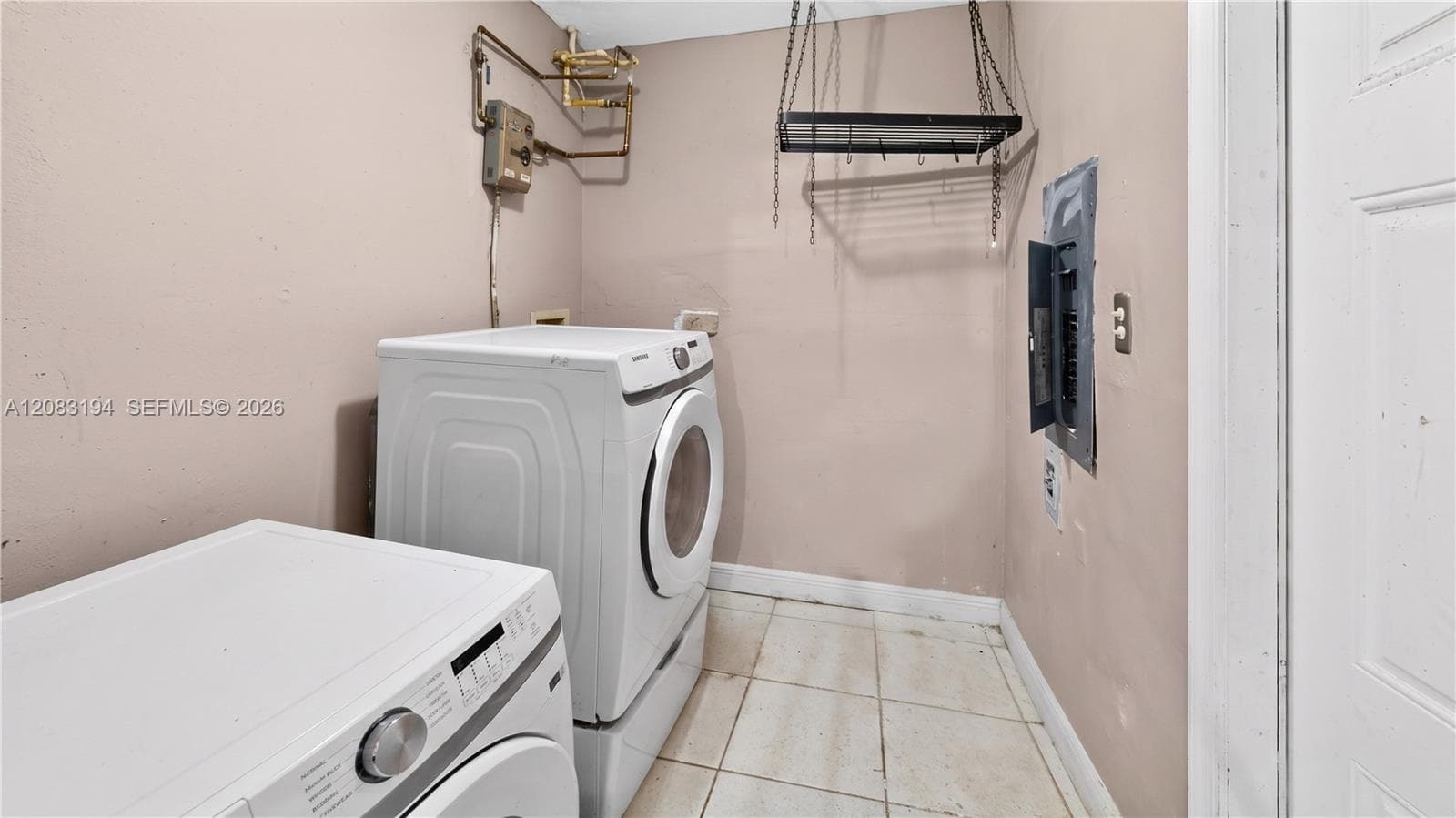 Utility area featuring light-toned tile flooring, an exposed electrical panel, and a wall-mounted hanging rack