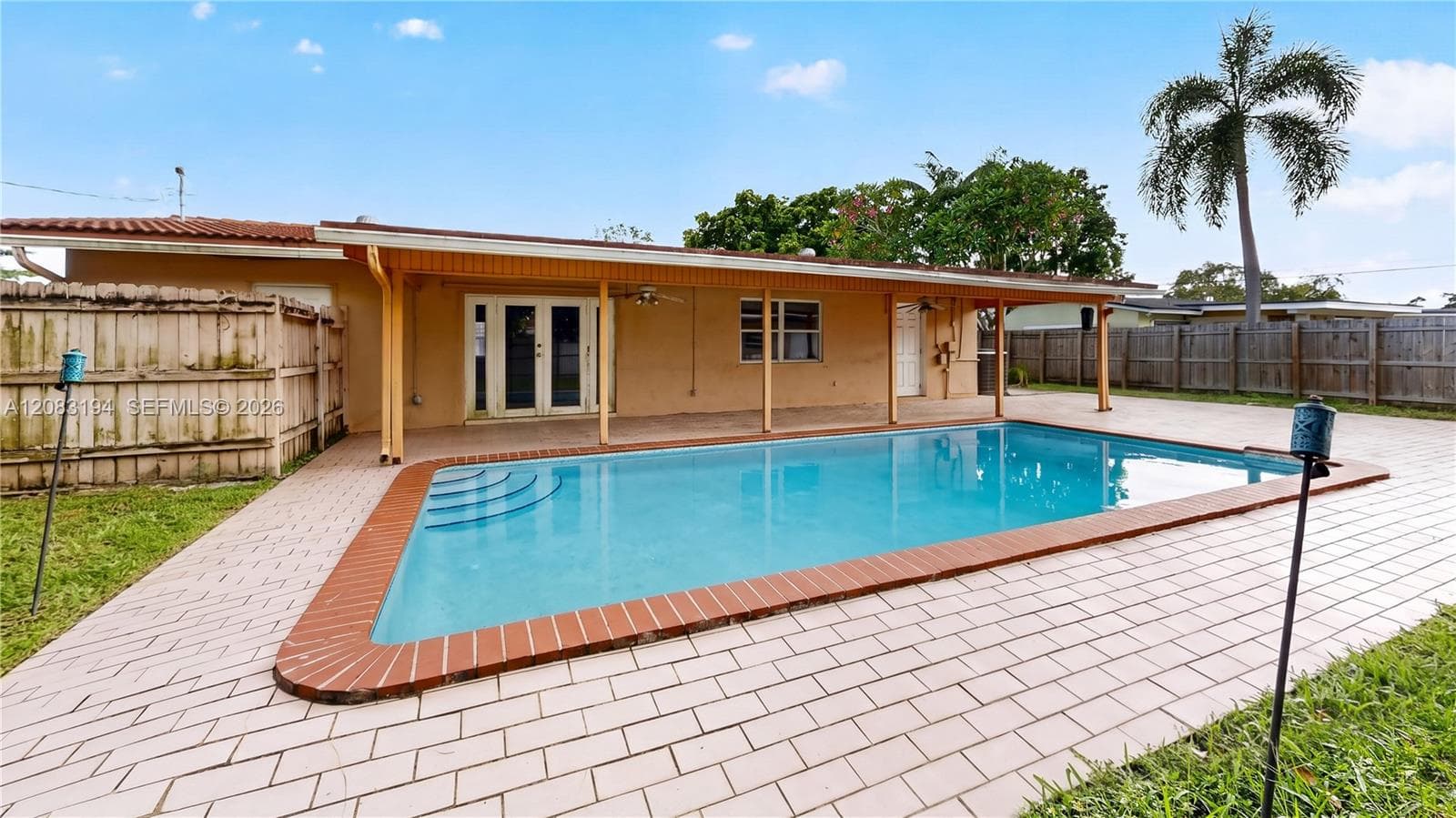 Rear exterior featuring an in-ground swimming pool with brick-style coping, expansive paver patio, covered porch, and wood-paneled privacy fencing