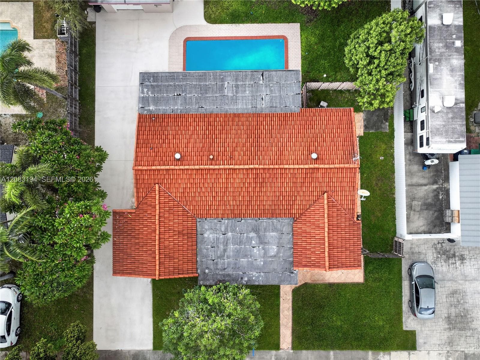 Aerial perspective featuring a tiled roof, concrete driveway, and an in-ground swimming pool set within a landscaped lot