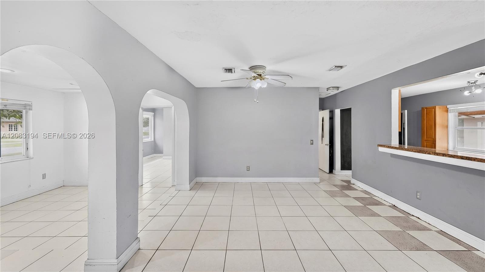 Interior space featuring arched architectural detailing, ceramic tile flooring, a ceiling-mounted light fixture with a fan, and a pass-through opening with a stone-finish countertop
