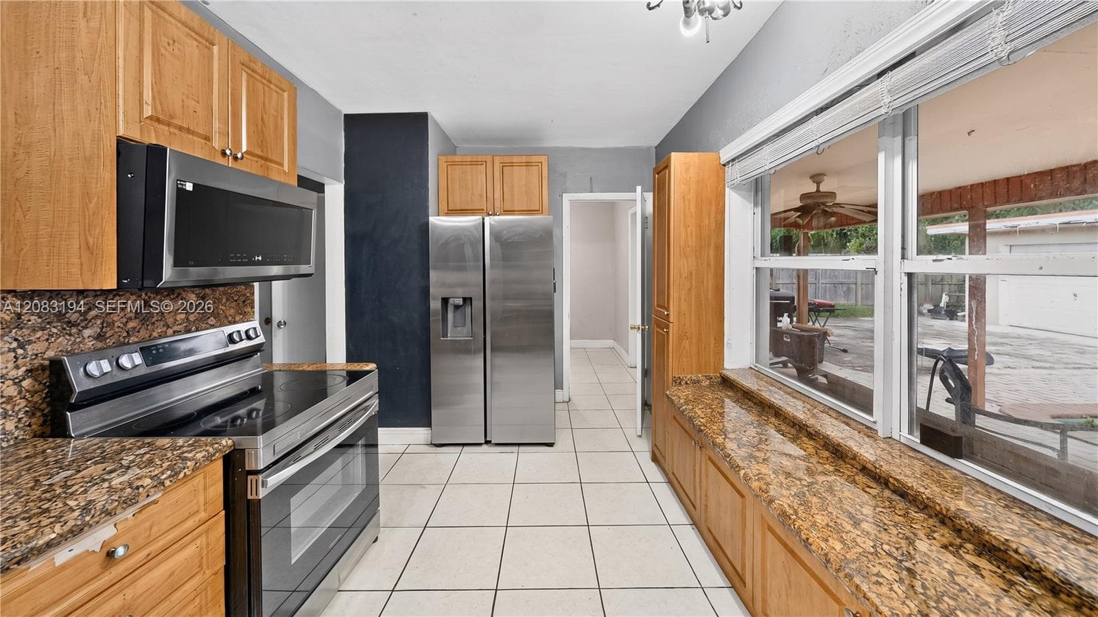 Kitchen featuring natural wood cabinetry, stone-finish countertops, stainless steel appliances, and large windows with integrated blinds