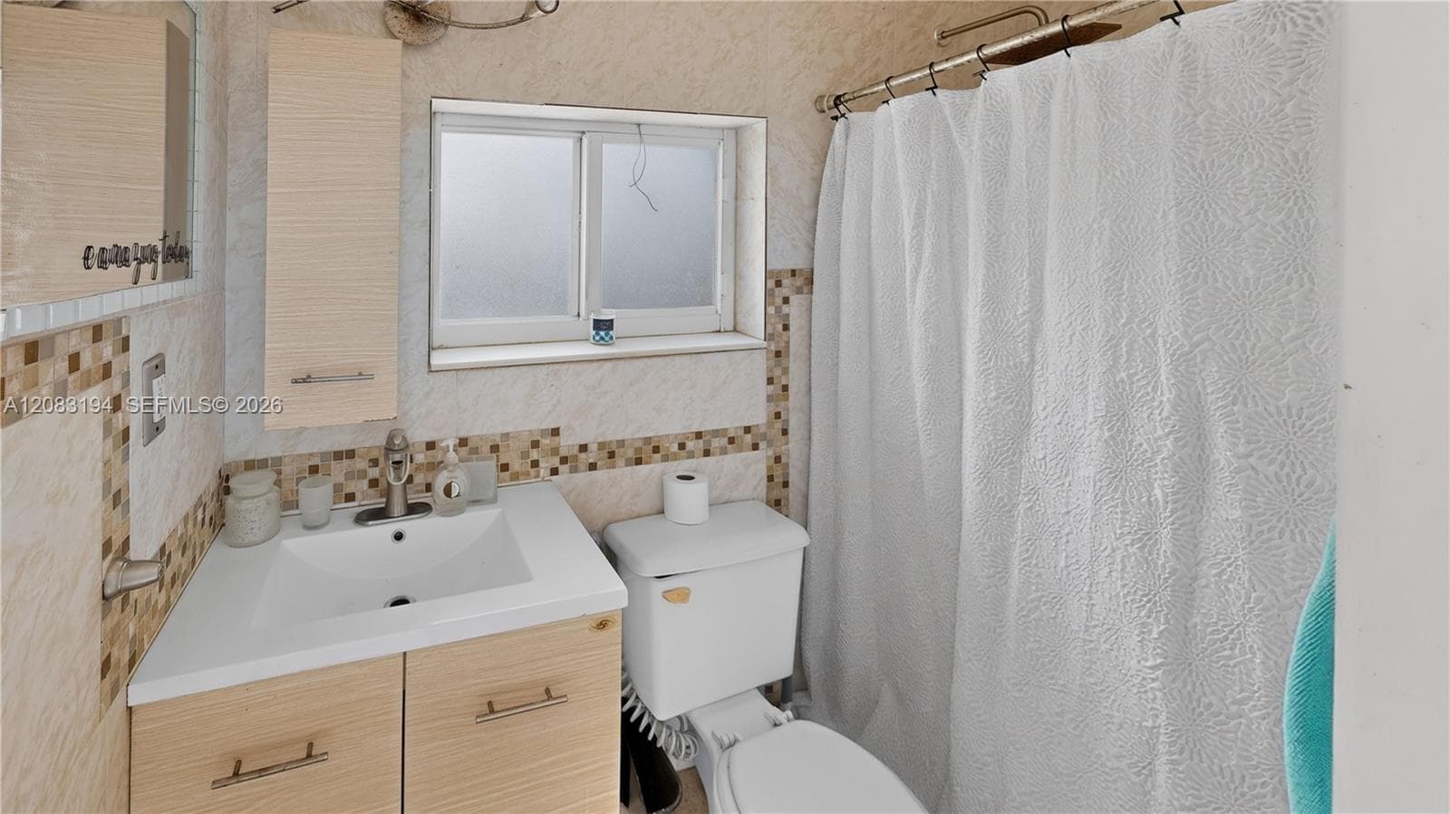 Bathroom featuring a wood-finish vanity with an integrated basin, wall-mounted cabinetry, mosaic tile backsplash, and a shower-tub combination