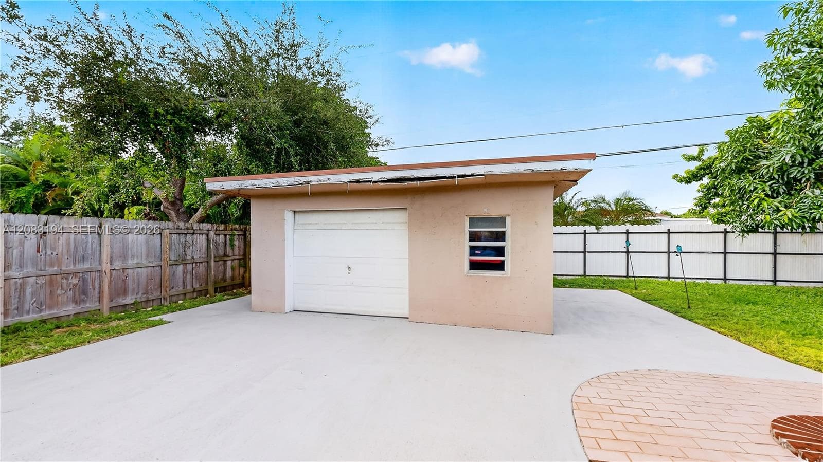 Detached garage structure with a single-car roll-up door, concrete driveway, and surrounding wood and vinyl perimeter fencing
