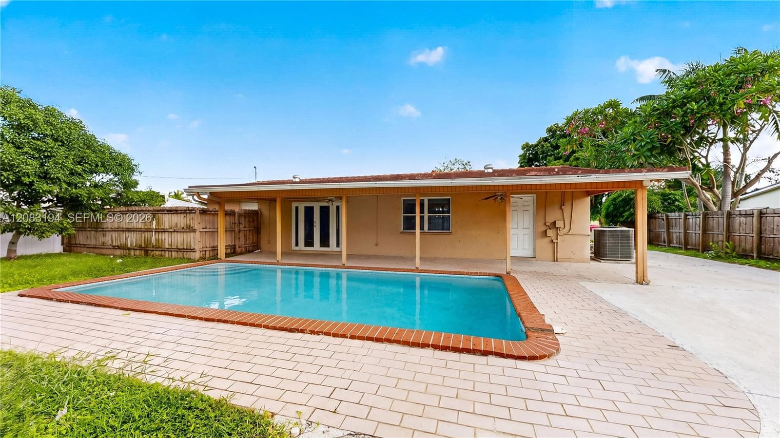 In-ground swimming pool with a brick-trimmed border, expansive paver patio, and covered porch area
