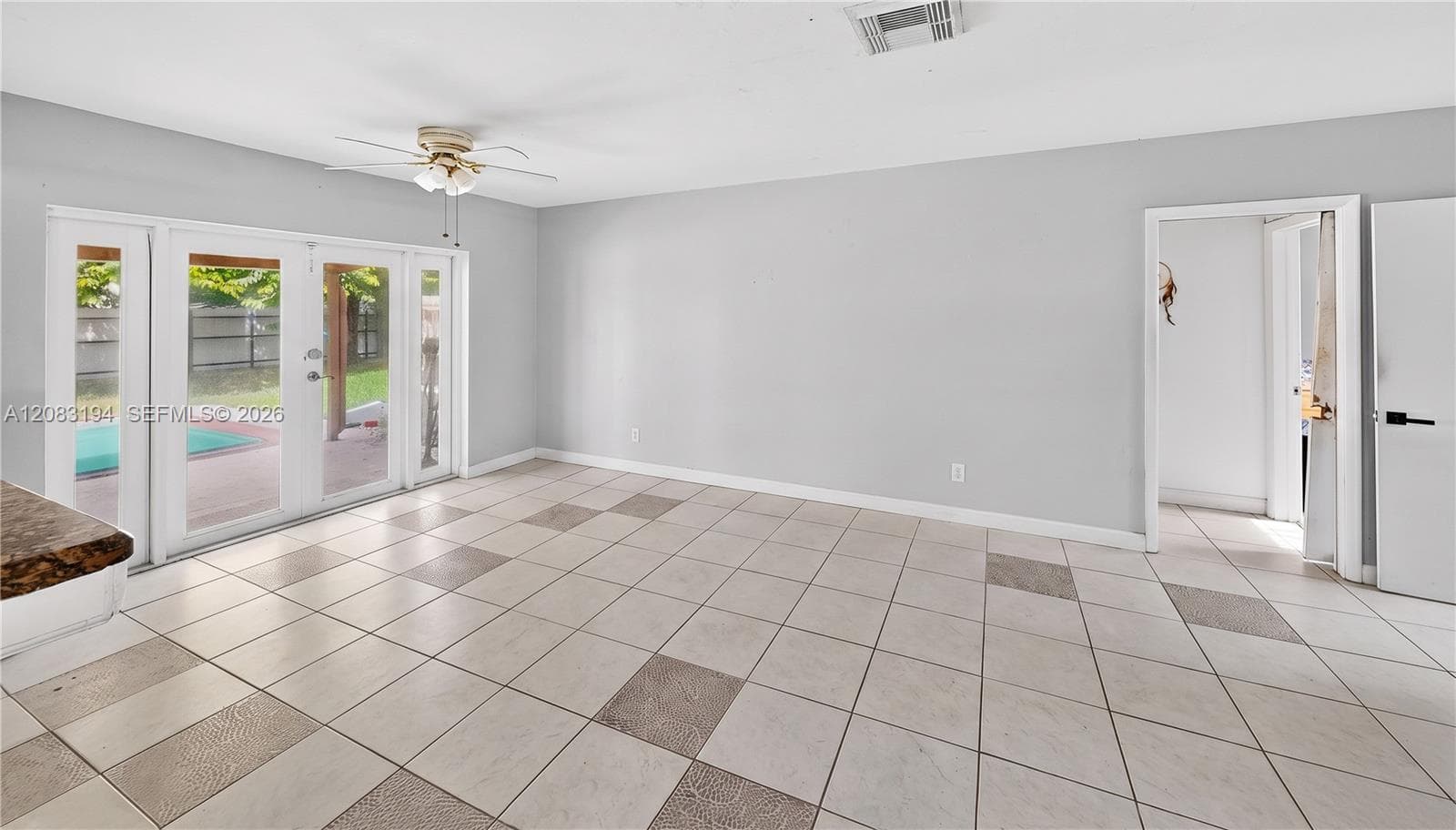Neutral-toned tile flooring, white-framed French doors, ceiling fan with integrated light fixture, and solid interior doors with matte black hardware