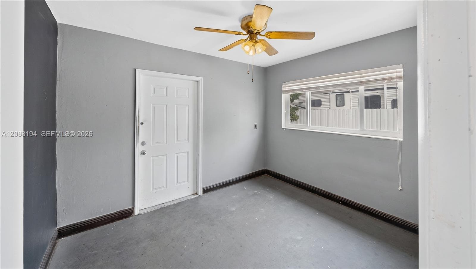 Interior space featuring grey-toned walls, a white-paneled door, a horizontal sliding window with integrated blinds, and a ceiling-mounted light fixture with a five-blade fan