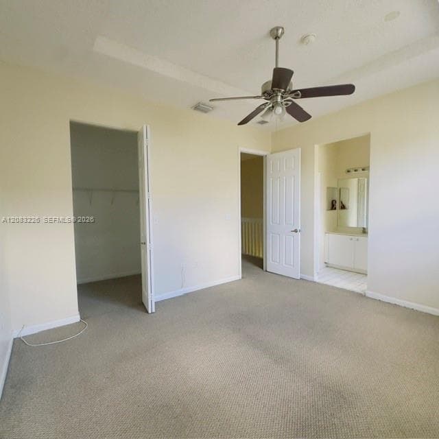 Interior space featuring a tray ceiling, wall-to-wall carpeting, a multi-blade ceiling fan, and a walk-in closet with built-in shelving