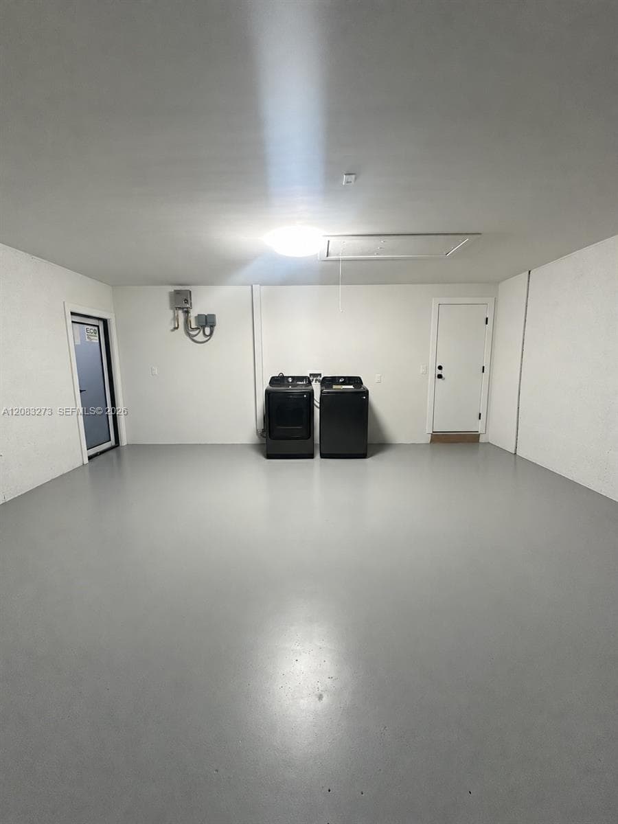 Expansive garage space featuring seamless epoxy flooring, smooth-finish walls, two pedestrian access doors, and an attic access hatch