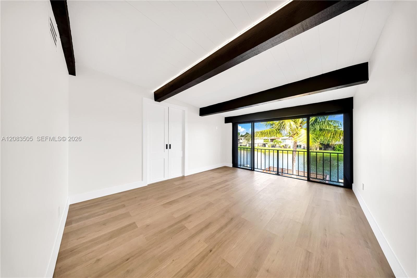 Wood-finish flooring, exposed ceiling beams, and dual sliding glass doors opening to a waterfront balcony