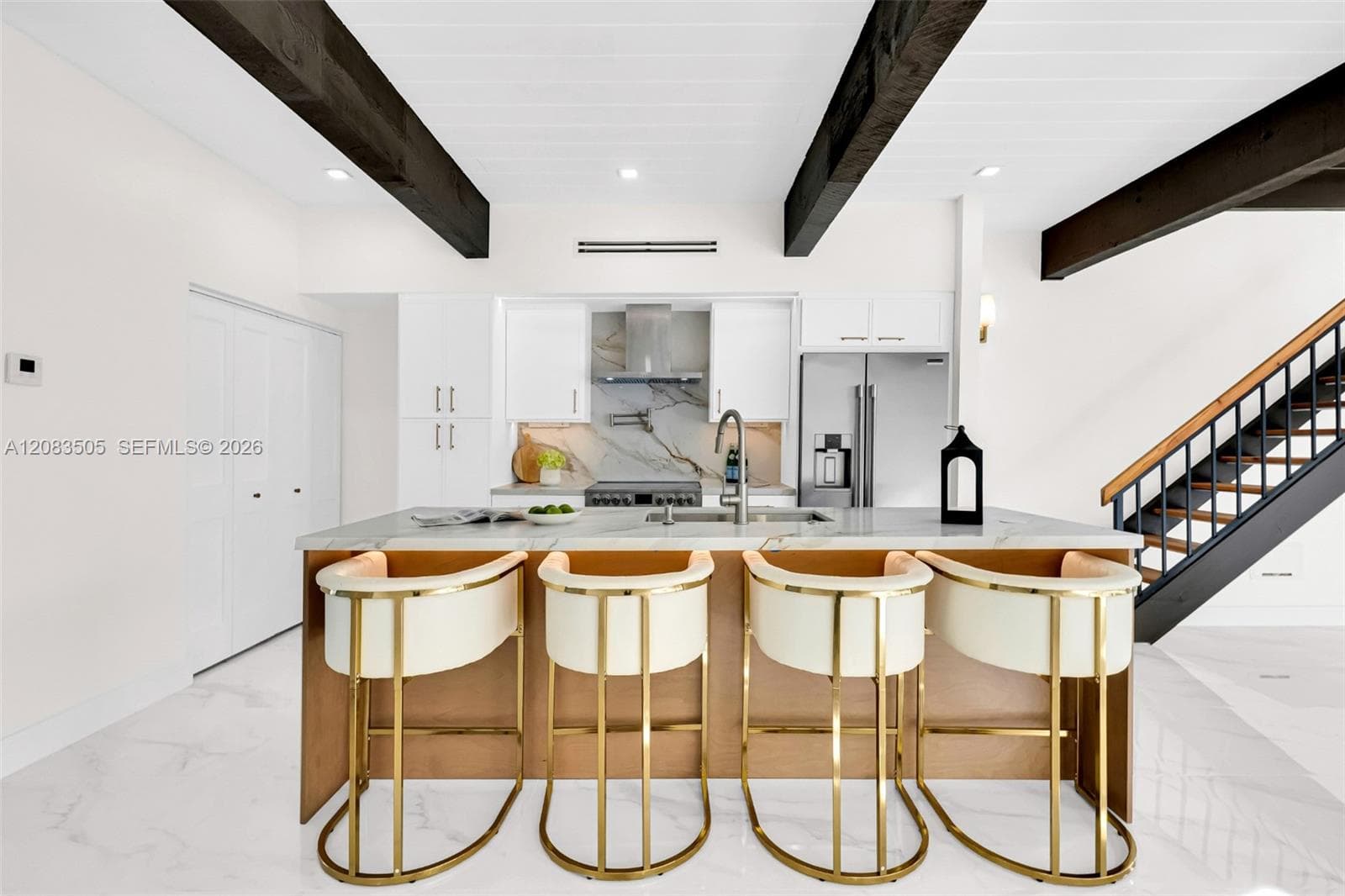 Kitchen featuring dark cedar wood-finish ceiling beams, white slim shaker-style cabinetry, stone-finish countertops, stainless steel appliances, and large-format tile flooring