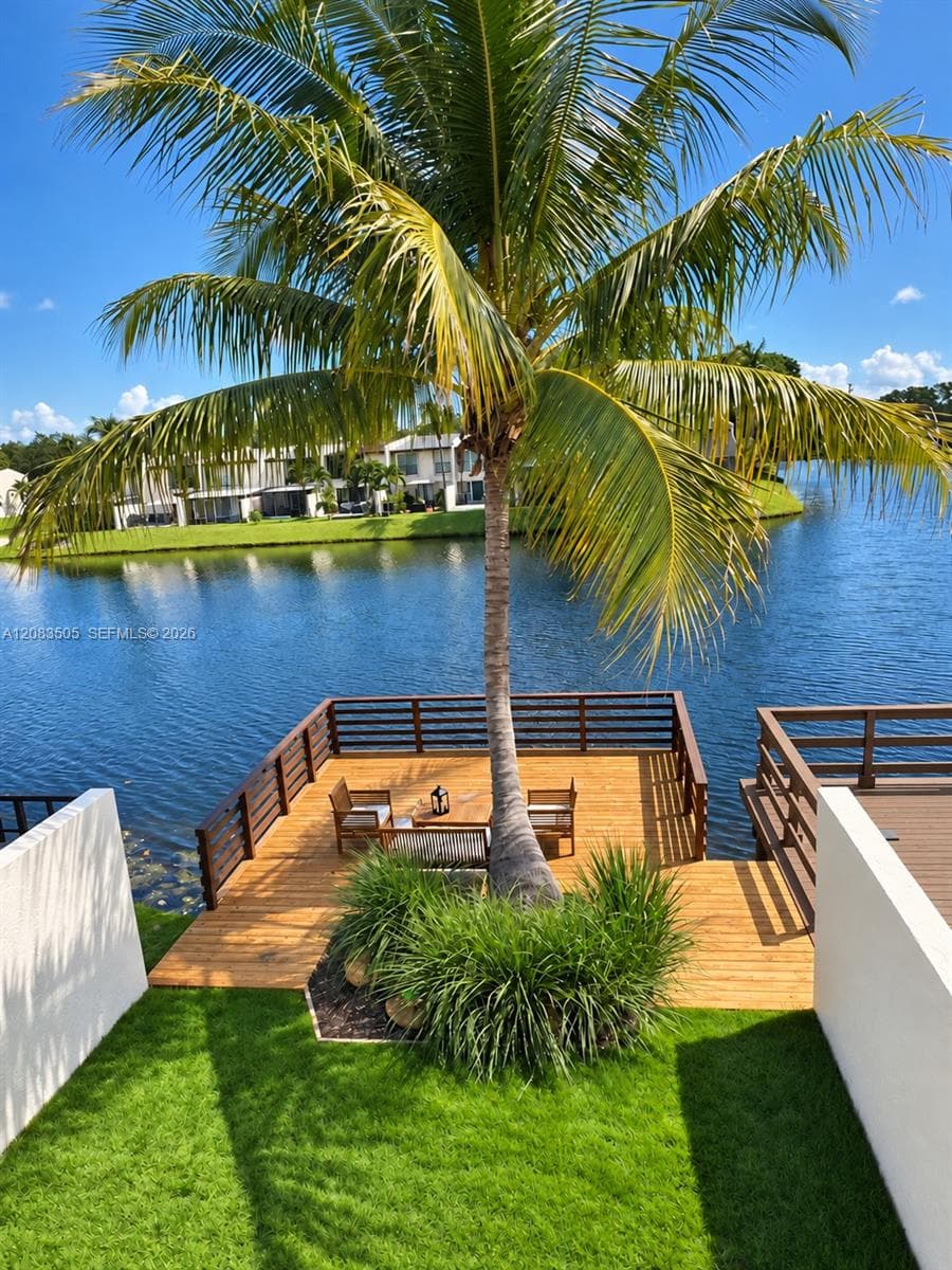 Waterfront wood deck featuring dark-toned horizontal railings and integrated landscaping with a mature palm tree and manicured lawn