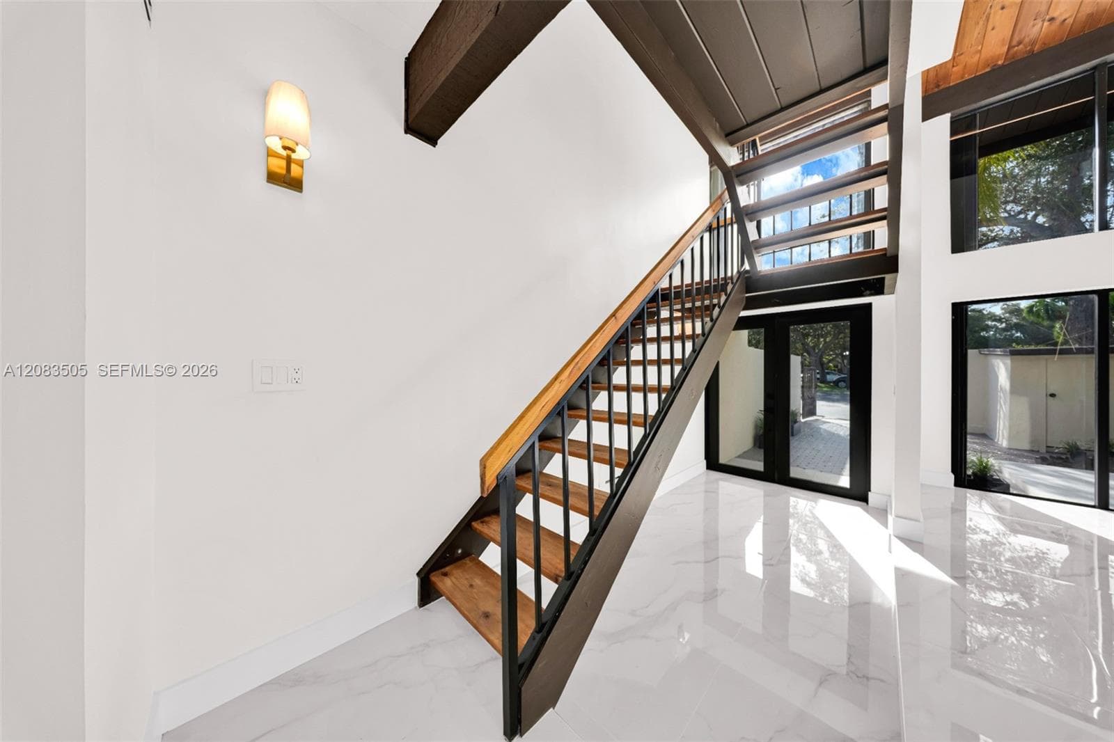 Staircase featuring open wood treads, black metal railings, and a wood handrail, polished white tile flooring, exposed dark wood ceiling beams, and floor-to-ceiling glass paneling