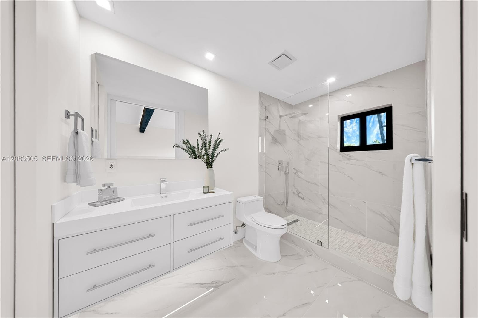 Bathroom featuring a white floating dual-drawer vanity with an integrated sink, floor-to-ceiling stone-style tile shower surround with a glass enclosure, and stone-style flooring