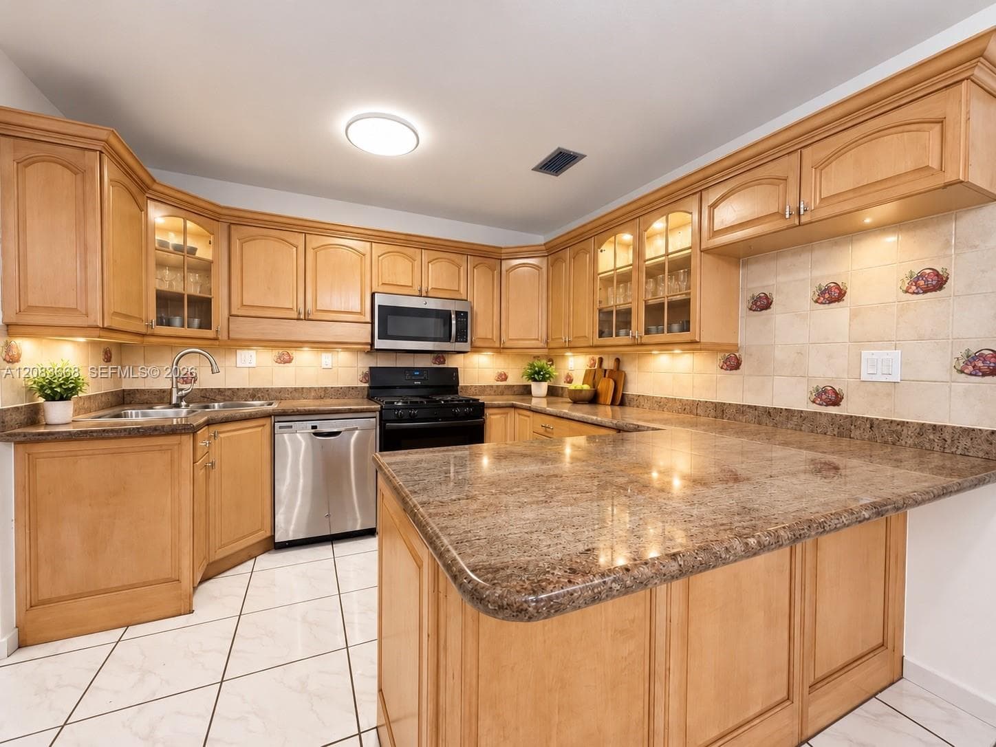 Kitchen featuring wood cabinetry, integrated stainless steel appliances, speckled countertops, and a tiled floor