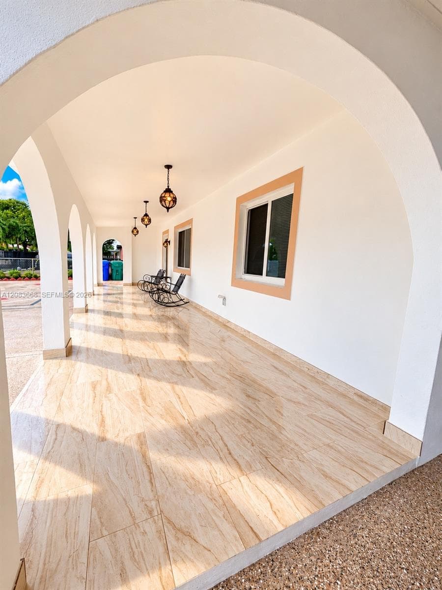 Arched covered walkway featuring large-format tile flooring, recessed lighting, decorative pendant lights, and framed windows
