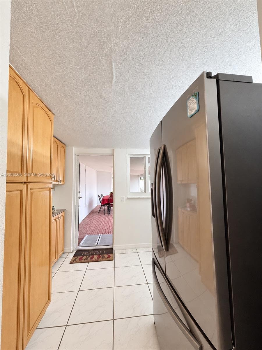 White tile flooring, stainless steel refrigerator, light wood-finish cabinetry, and built-in window