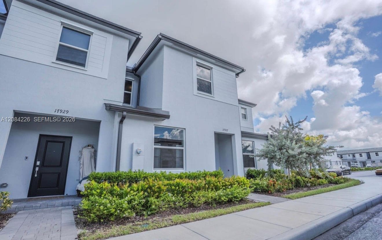 Two-story stucco exterior featuring horizontal siding accents, dark-framed windows, a covered entryway, and professionally landscaped shrubbery