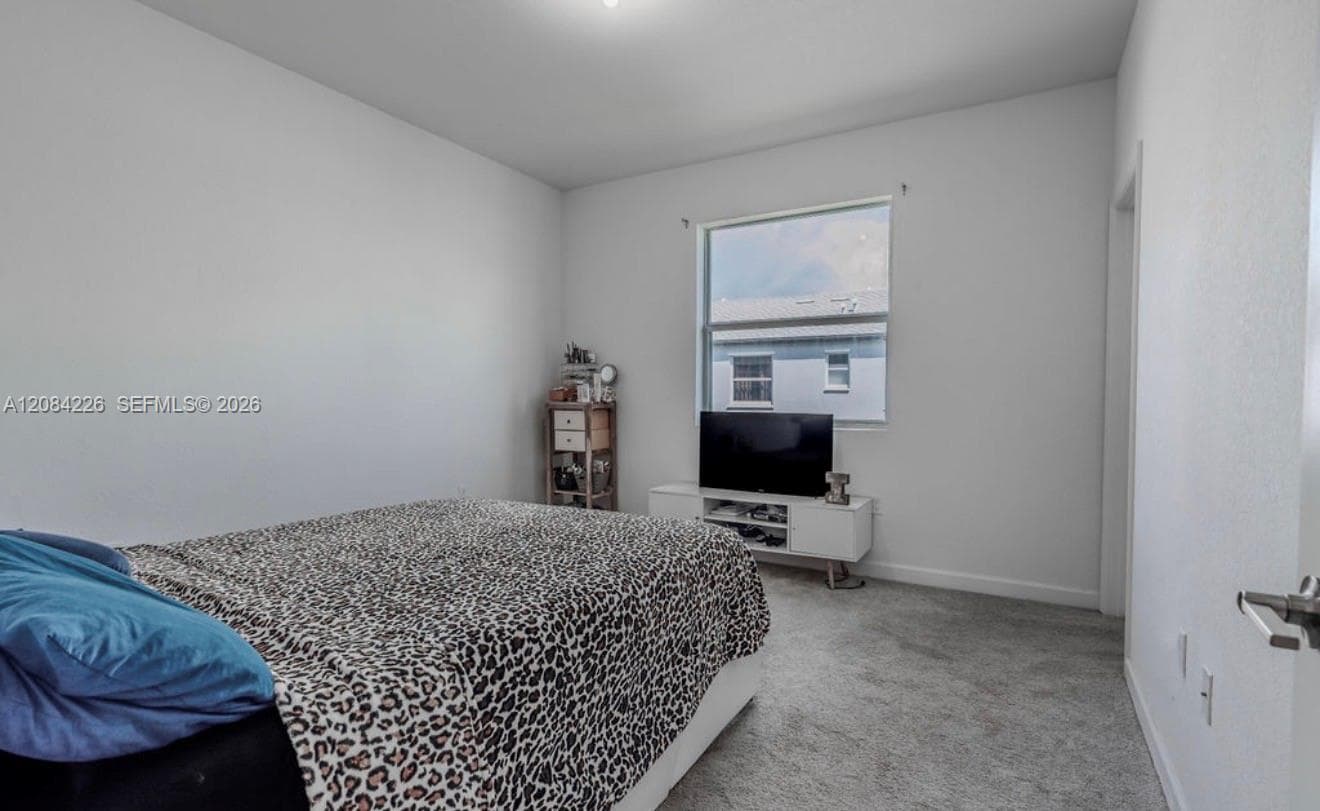 Neutral-toned interior space featuring light-colored wall paint, plush carpeting, and a large window