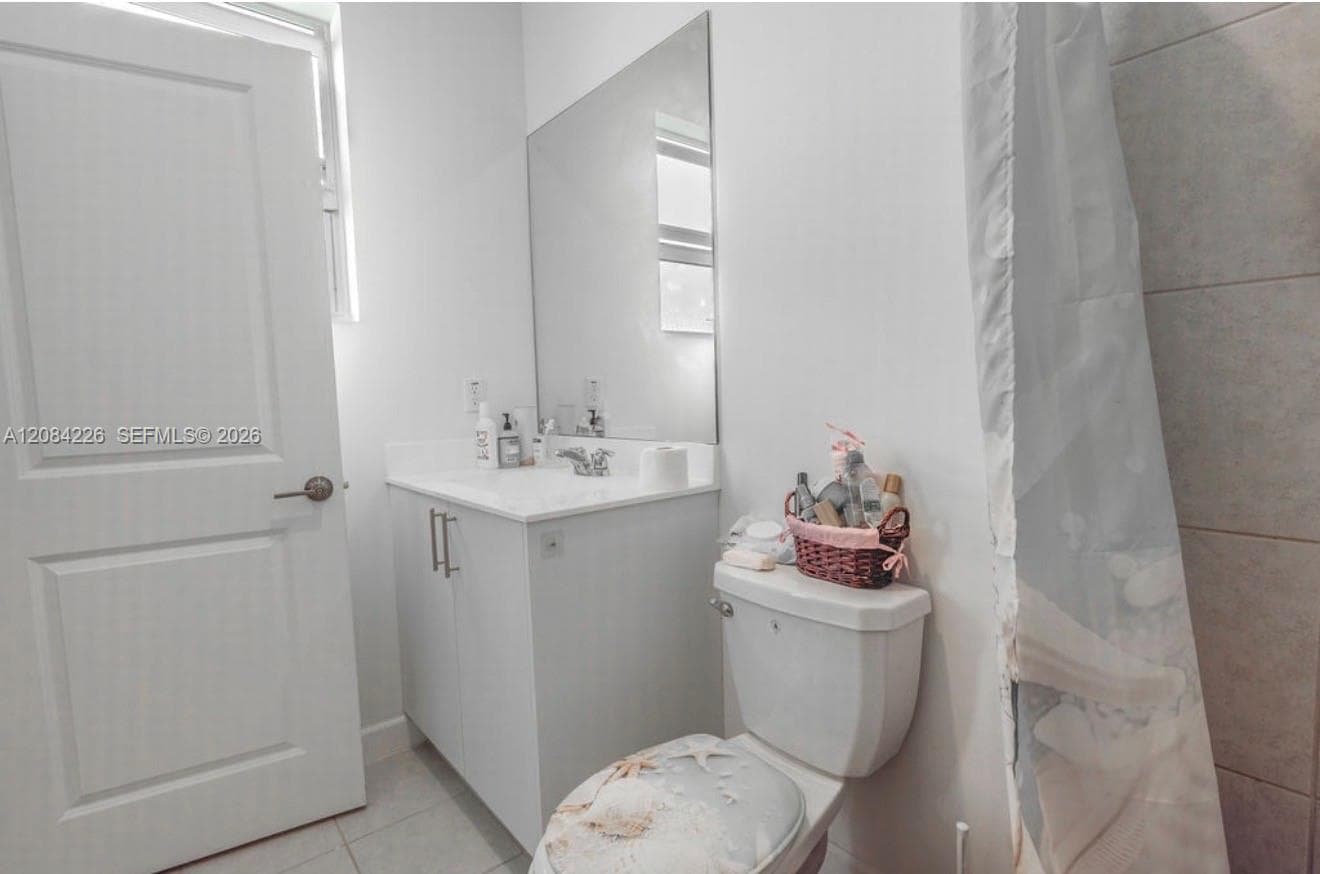 White vanity cabinet with a solid surface countertop, integrated basin, frameless wall-mounted mirror, and tiled shower surround